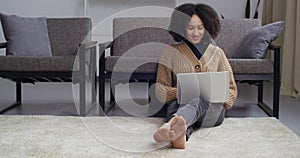 Afro american student teenager mixed race girl black woman sitting on floor at home near sofa working remote with laptop