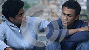 Afro-American teen boy with bruised face hugging brother sitting alone on stairs