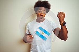 Afro american tourist man holding Argentinian Argentina flag over isolated white background annoyed and frustrated shouting with