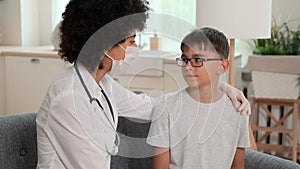 Afro american woman doctor in mask supports sick child with hand on shoulder