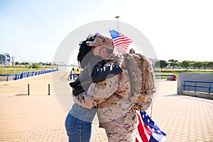 Afro-American woman and soldier who has just returned from war on a mission embrace each other tightly. The woman is holding the