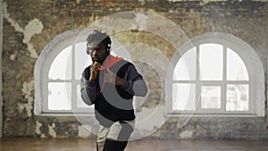 Afro american young male boxer practicing shadow boxing in headphones in bright hall
