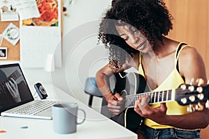 afro american young woman learning to play guitar with online lessons