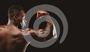 Afro bodybuilder showing strong biceps on black background