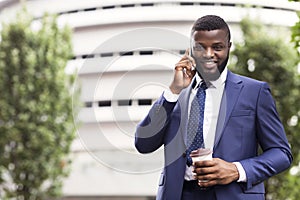 Afro Businessman Having Coffee And Talking On Mobile Phone Outdoors