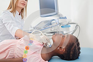 Afro child lying when doctor scanning her neck.