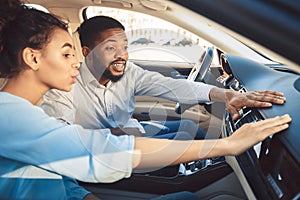 Afro couple at car showroom touching dash of new auto