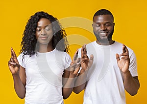 Afro couple closing eyes and crossing fingers with hope