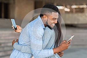 Afro couple cuddling outdoors and looking at smartphone screen over shoulder