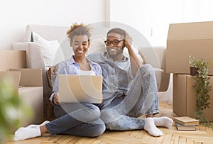 Afro Couple Using Laptop Sitting Among Moving Boxes At Home