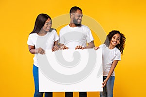 Afro family holding blank white advertising billboard at studio