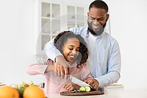 Afro father teaching daughter how to prepare salad