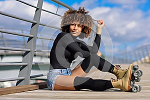 Afro hairstyle woman on roller skates sitting on urban bridge