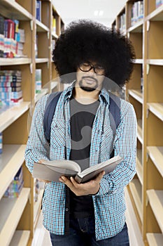 Afro male student reading a book at library