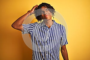 Afro man with dreadlocks wearing casual striped t-shirt over isolated yellow background confuse and wonder about question
