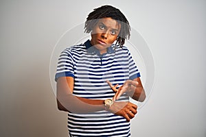 Afro man with dreadlocks wearing striped blue polo standing over isolated white background In hurry pointing to watch time,