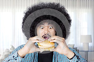 Afro man eating a big cheeseburger at home