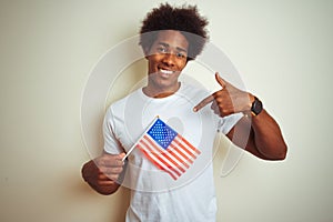 Afro man holding United Estates of America USA flag standing over isolated white background with surprise face pointing finger to