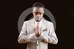 Afro man with joined hands and closed eyes on the isolated black background