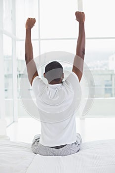 Afro man waking up in bed and stretching his arms