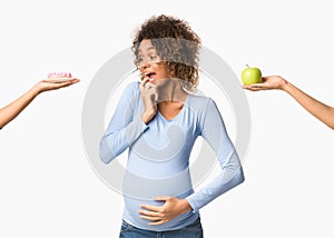 Afro pregnant woman choosing between sweet and fruit