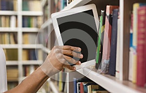 Afro student placing digital tablet on bookshelf