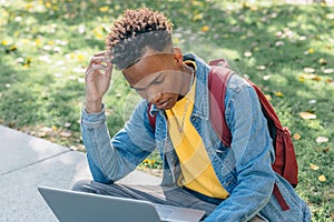 Afro styled young man looks worriedly at his computer in a park