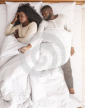 Afro woman annoyed by her boyfriend sprawled out all over bed