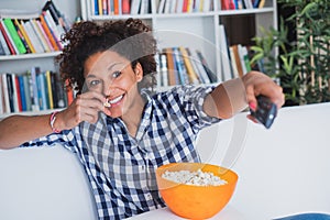 Afro woman sitting at home with remote control watching tv