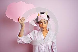 Afro woman wearing pajama and mask holding speech bubble over isolated pink background with a confident expression on smart face