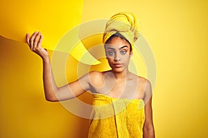 Afro woman wearing towel after shower holding speech bubble over isolated yellow background with a confident expression on smart