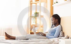 Afro Woman Working On Laptop Computer Lying In Bed Indoor