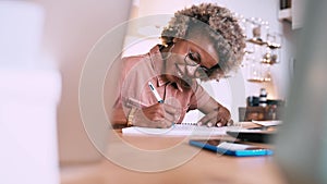 Afro woman writing in a notebook at home on an office table