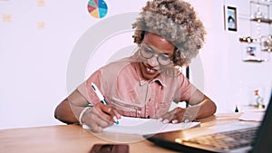 Afro woman writing in a notebook at home on an office table