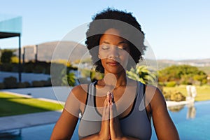 Afro young african american woman with hands clasped and eyes closed exercising in backyard