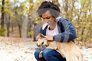 Afroamerican girl in autumn park playing with her dog