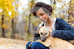 Afroamerican girl in autumn park playing with her dog