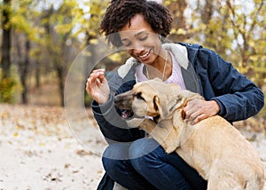 Afroamerican girl in autumn park playing with her dog