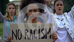 Afroamerican girl holding No racism sign, activists chanting Human rights slogan