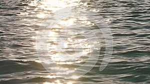 Afternoon or evening sun shines to calm sea, light reflecting on small waves, slow motion closeup detail