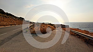 Afternoon sun shines on asphalt road leading down to beach, sea in distance - typical landscape in Karpas region of