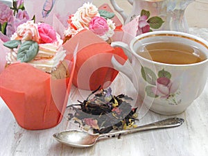 Afternoon tea with flowers cupcakes, vintage teacup, old silver spoon and petals brew on shabby table, tender colors of spring