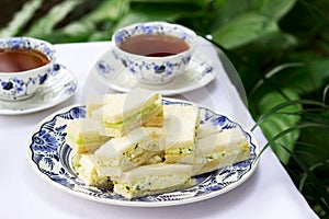 Afternoon tea in the garden, finger sandwiches with cucumber and egg salad and tea on a light background.