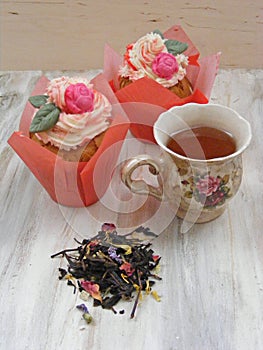 Afternoon tea with roses cupcakes in vintage teacup ans flowers brew on shabby table colors of spring