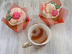 Afternoon tea with roses cupcakes in vintage teacup on shabby table flat wiev