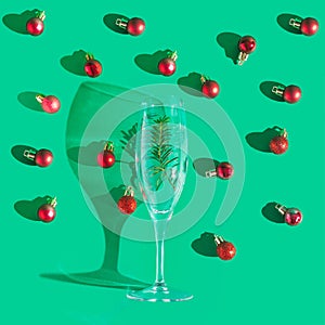 Afterparty Christmas inspired concept. Sunny shadow with champagne glass, green spruce and many shiny red bulbs around. Flat lay