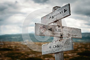 Against all odds text on wooden rustic signpost outdoors in nature/mountain scenery.