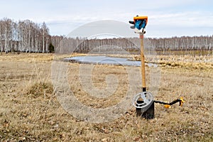 Against the backdrop of the lake and the field there are staked shovel in the ground on the shovel metal detector, wounding the sp