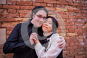 Against the backdrop of a red brick wall, young couple holds each other tightly looking in the same direction