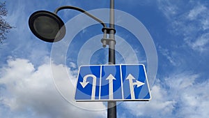 Against the background of a blue sky with white clouds, a lamppost with car turn signs